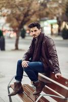 jeune homme réfléchi assis sur un banc urbain. photo