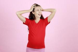 jeune et belle femme enceinte en t-shirt rouge à l'aide de mains tenant sa tête avec un geste furieux et stressant photo