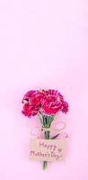 mai fête des mères idée concept photographie - beaux oeillets en fleurs attachés par un arc avec une carte de texte kraft isolée sur une table moderne et lumineuse, espace de copie, mise à plat, vue de dessus photo