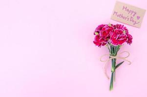 mai fête des mères idée concept photographie - beaux oeillets en fleurs attachés par un arc avec une carte de texte kraft isolée sur une table moderne et lumineuse, espace de copie, mise à plat, vue de dessus