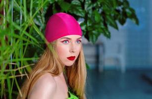 portrait d'une belle femme blonde séduisante athlétique avec maquillage en bonnet de bain et costume dans la piscine avec des fleurs et des plantes vertes photo