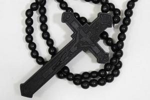 perles de chapelet avec croix en bois noir sur fond blanc, mise au point sélectionnée sur le christ, faible profondeur de champ. photo