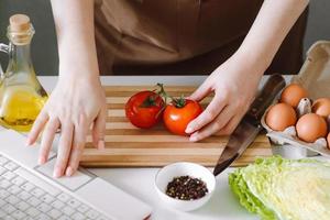 femme blogueuse préparant une salade de légumes diététiques. cours de cuisine en ligne, en utilisant un ordinateur portable dans la cuisine. photo
