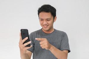 wow visage et se sentir heureux d'un jeune homme asiatique en t-shirt gris se faire surprendre sur le smartphone. photo