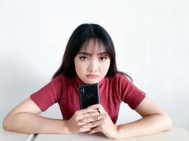 belle fille asiatique réfléchit et pense en regardant vers l'extérieur dans le smartphone sur le fond blanc isolé photo