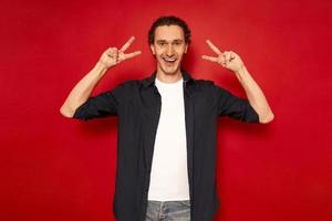 portrait d'un homme séduisant, souriant et d'une maturité enfantine, vêtu d'une chemise bleue avec des signes souriants en forme de V surlignés en rouge sur fond de studio. concept - peuple, victoire, victoire, célébration photo