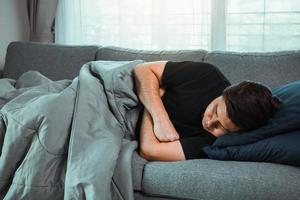 un homme asiatique ressent la maladie alors qu'il avait froid allongé sur le canapé et portant une couverture chez lui. photo