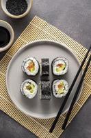 sushi sur assiette ronde avec baguettes, sauce soja. Gingembre. petits pains maison au saumon, avocat et concombre.