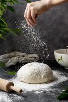 cuisson du pain maison au levain. tamiser la farine sur la pâte à pain crue sur la table, fond sombre, mise au point sélective. photo