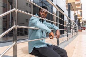 pensif jeune homme noir assis près de l'entrée du bâtiment dans la rue photo