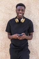 contenu homme afro-américain souriant tout en envoyant des messages sur un smartphone dans la rue photo