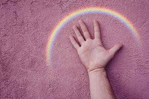 main avec un arc-en-ciel sur le mur rose. symbole lgbt photo