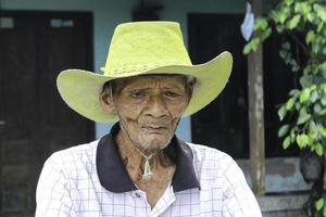 un portrait d'un vieux fermier indonésien portant un chapeau jaune avec un vieux vélo photo