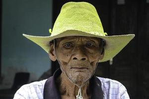 un portrait d'un vieux fermier indonésien portant un chapeau jaune avec un vieux vélo photo