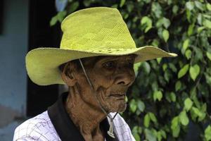 un portrait d'un vieux fermier indonésien portant un chapeau jaune avec un vieux vélo photo