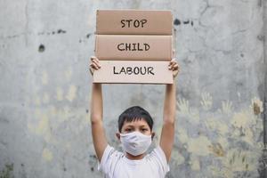 garçon asiatique en masque médical levant le tableau des lettres dit stop à la campagne contre la maltraitance des enfants avec empreinte de la main dans le fond du mur de ciment photo