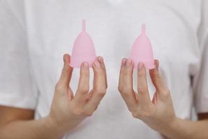 gros plan sur une main de femme tenant des coupes menstruelles de tailles différentes. concept de santé des femmes, alternatives zéro déchet photo