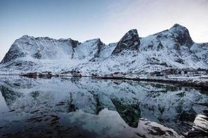 chaîne de montagnes de neige avec réflexion scandinave rorbuer sur la côte à lofoten photo