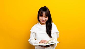 photo d'une fille asiatique souriante en lisant un livre tout en souriant sur fond jaune concept de lecture de livre une petite fille qui aime lire des livres