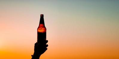 main et bouteille de bière d'une fille tenant une bouteille de bière au bord de la mer buvant de la bière seule faire la fête et socialiser lors d'une journée de détente photo