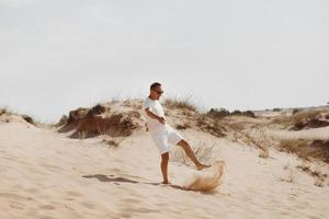 jeune bel homme en vêtements légers et lunettes de soleil dans le désert. concept de relaxation de liberté. place pour le texte ou la publicité photo