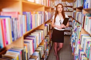 fille brune à la bibliothèque avec dossier de documents, porter sur chemisier blanc et mini jupe noire. femme d'affaires sexy ou concept d'enseignant. photo