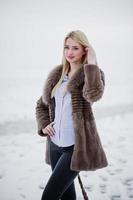 portrait de jeune fille blonde élégance dans un fond de manteau de fourrure rivière brumeuse sur la glace d'hiver. photo