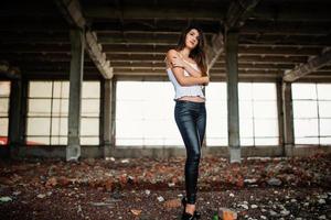 portrait d'une jeune fille brune mignonne portant un pantalon en cuir noir et un chemisier blanc posé sur un lieu abandonné. photo