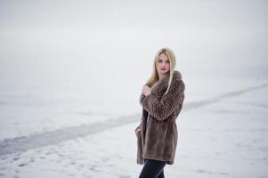 portrait de jeune fille blonde élégance dans un fond de manteau de fourrure rivière brumeuse sur la glace d'hiver. photo