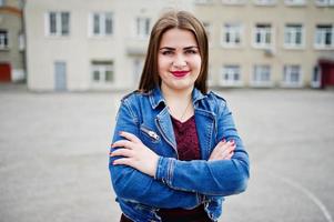 jeune adolescente potelée portant une robe rouge et une veste en jean posée contre l'arrière-cour de l'école. photo