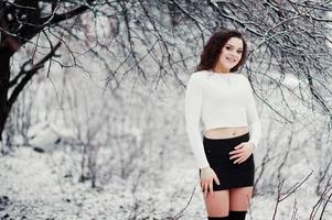 fond de fille brune bouclée chute de neige, usure sur mini jupe noire et bas de laine. modèle sur l'hiver. portrait de mode par temps neigeux. photo tonique instagram.