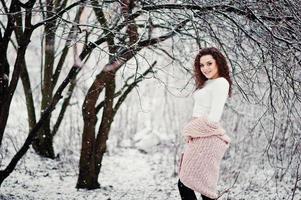 fond de fille brune bouclée chute de neige, porter sur un pull en tricot chaud, une mini jupe noire et des bas de laine. modèle sur l'hiver. portrait de mode par temps neigeux. photo tonique instagram.