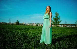 femme dans une belle robe longue turquoise posant sur un pré sur l'herbe. photo