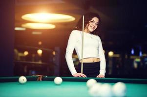 jeune fille frisée posée près de la table de billard. modèle sexy à mini mini jupe noire jouer au billard russe. jouer au jeu et au concept amusant. photo