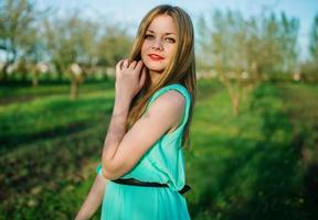 femme dans une belle longue robe turquoise posant sur un pré dans le jardin fruitier. photo