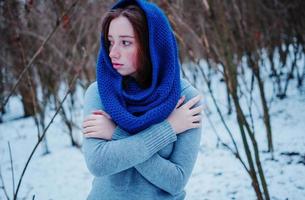 portrait de jeune fille aux cheveux roux avec des taches de rousseur portant une écharpe en laine tricotée bleue en journée d'hiver. photo