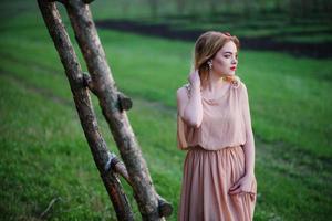 yong élégance fille blonde à robe rose sur l'escalier en bois de fond de jardin. photo