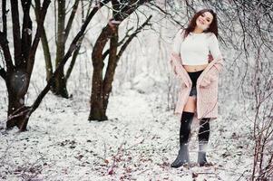 fond de fille brune bouclée chute de neige, porter sur un pull en tricot chaud, une mini jupe noire et des bas de laine. modèle sur l'hiver. portrait de mode par temps neigeux. photo tonique instagram.