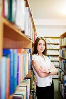 fille brune à la bibliothèque, porter un chemisier blanc et une mini jupe noire. femme d'affaires sexy ou concept d'enseignant. photo