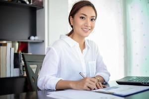 belles femmes d'affaires asiatiques vérifiant le document et utilisant un ordinateur portable pour travailler à la maison photo