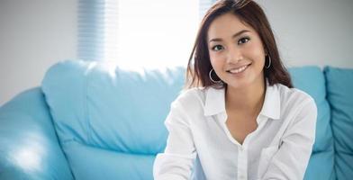 femmes asiatiques assises sur un canapé et elle sourit heureuse à la maison photo
