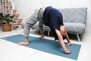 Garçon asiatique sur tapis bleu avec pose de yoga à la maison photo