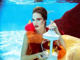 portrait de mode sous-marine de la belle jeune femme blonde en robe rouge avec lampe photo
