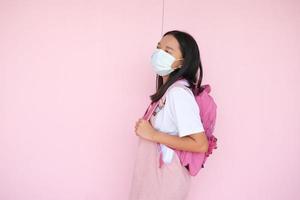 étudiant jeune fille porter un masque avec sac à dos sur fond rose. photo