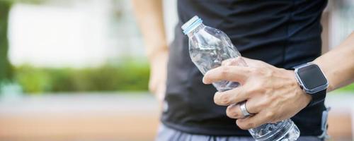 sportif asiatique actif se relaxant et buvant de l'eau en bouteille après une course ou une séance d'entraînement en plein air. un homme asiatique boit de l'eau pendant la pause de l'exercice. un homme en bonne santé qui s'efforce de faire de l'exercice cardio. photo