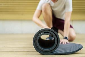 sportif asiatique actif déroule un tapis d'exercice sur le sol, corps sain et en forme d'homme de sport asiatique préparant un tapis de yoga d'entraînement pour le poids corporel et l'exercice cardio. photo