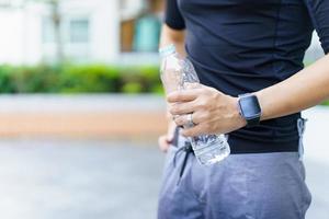 sportif asiatique actif se relaxant et buvant de l'eau en bouteille après une course ou une séance d'entraînement en plein air. un homme asiatique boit de l'eau pendant la pause de l'exercice. un homme en bonne santé qui s'efforce de faire de l'exercice cardio. photo