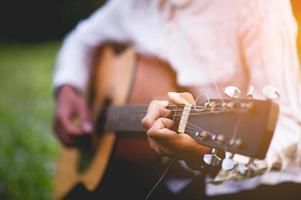 la main de l'homme joue de la guitare acoustique, joue de la guitare dans le jardin seul, heureusement et aime la musique. photo