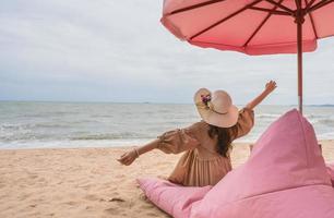 femme heureuse bras stretche sur une chaise rose dans un café de luxe sur la plage photo