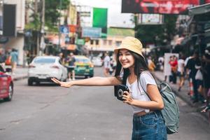 une jeune femme asiatique tient un appareil photo instantané et appelle un taxi à bangkok, en thaïlande.